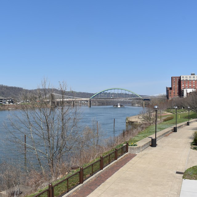 paved walking path near river with bridge in view