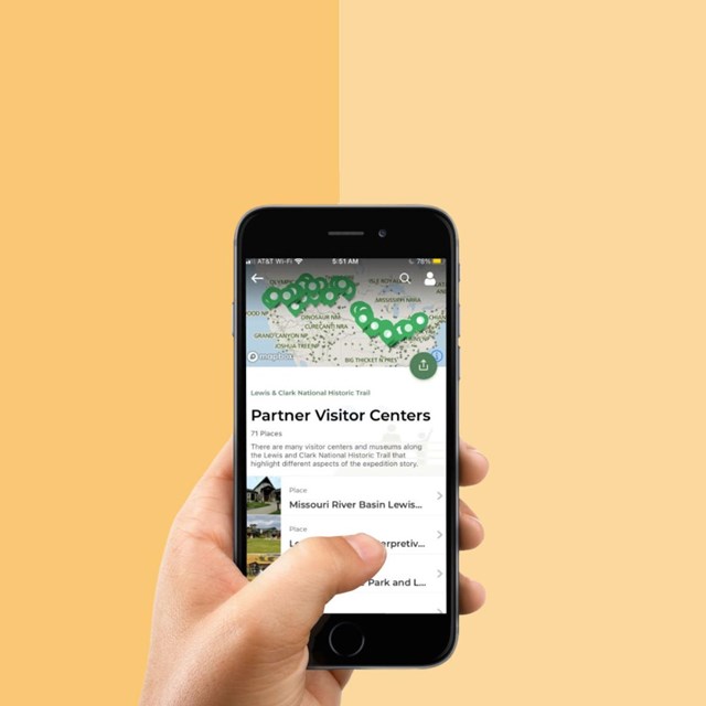 Hand holding phone with app on screen. App shows Lewis and Clark Trail map and visitor centers.