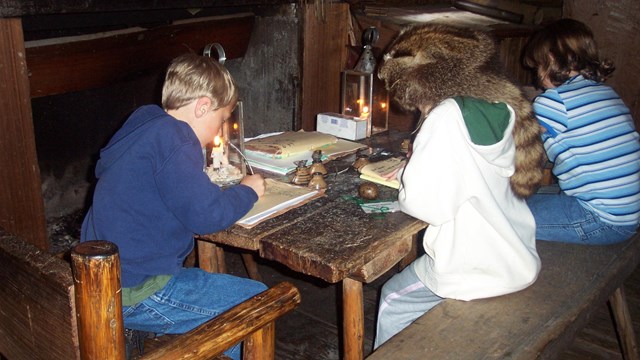Students in Captain's Quarters sitting at a table writing with quill pens