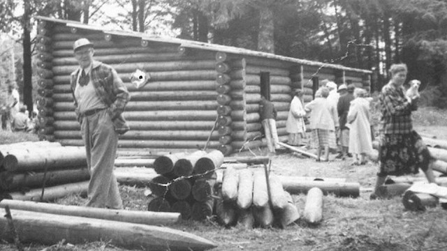 Historic photos of the fort clatsop rebuild with a man standing in front of a pile of logs