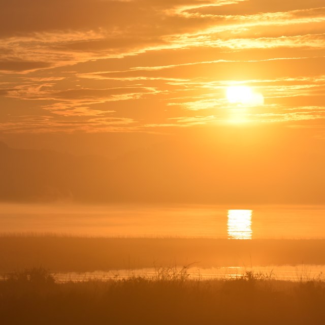 Sun and body of water with sun reflecting. Photo has intense orange tint due to smoke. 