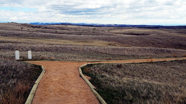 Deep Ravine Trail with two markers on the edge of the trail and mixed grass prairie on both sides.