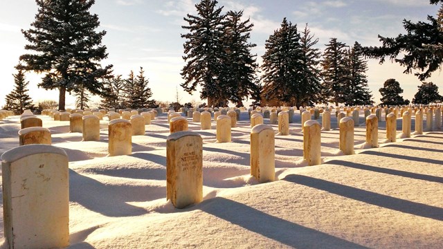 Snow blankets the ground around the headstones as the sun sets on the Custer National Cemetery. 