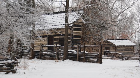 Log cabin and split rail fence all covered with snow.