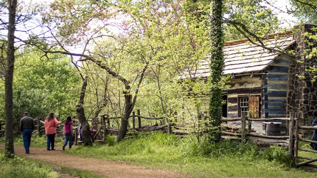 Family on trail in front of log cabin surrounded by trees
