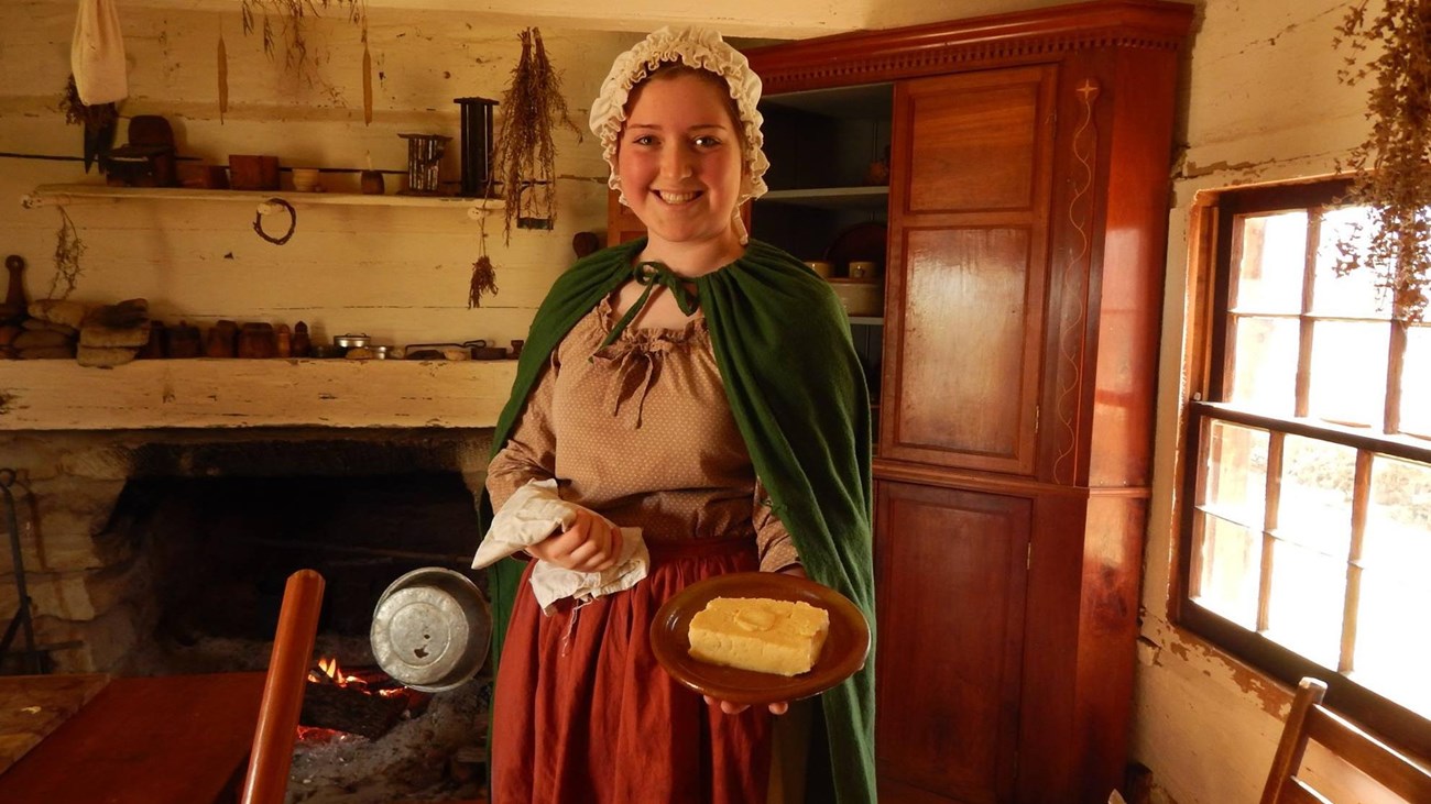 Smiling woman inside log cabin with white walls holding square of butter on a plate
