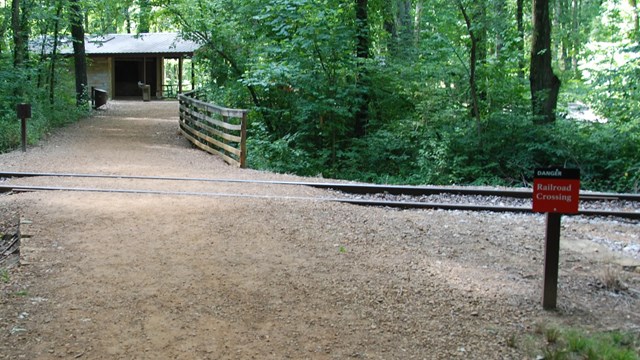 Trail crossing railroad tracks, warning sign, shelter in background