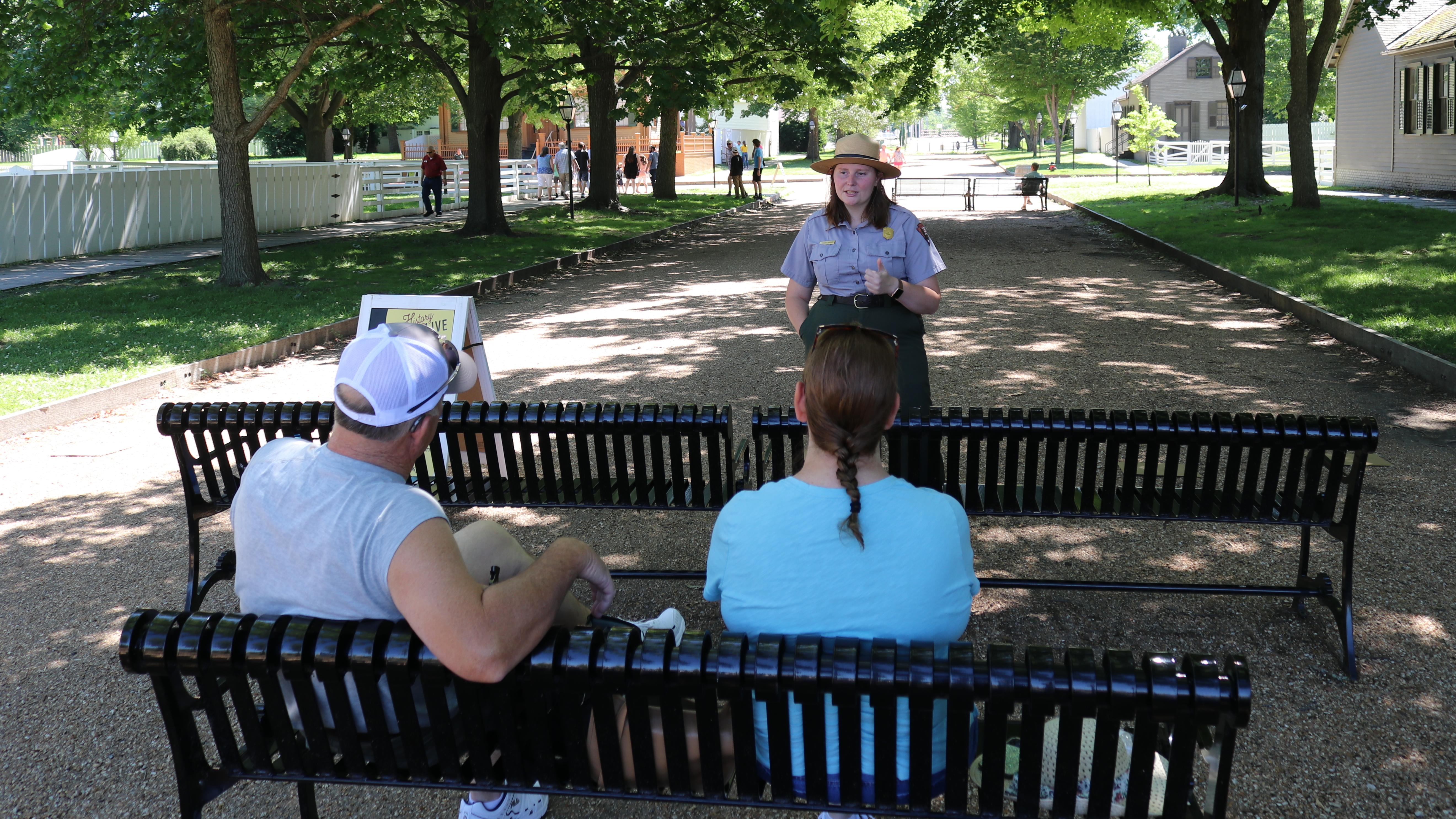 A park ranger talking to two people sitting on black benches. 