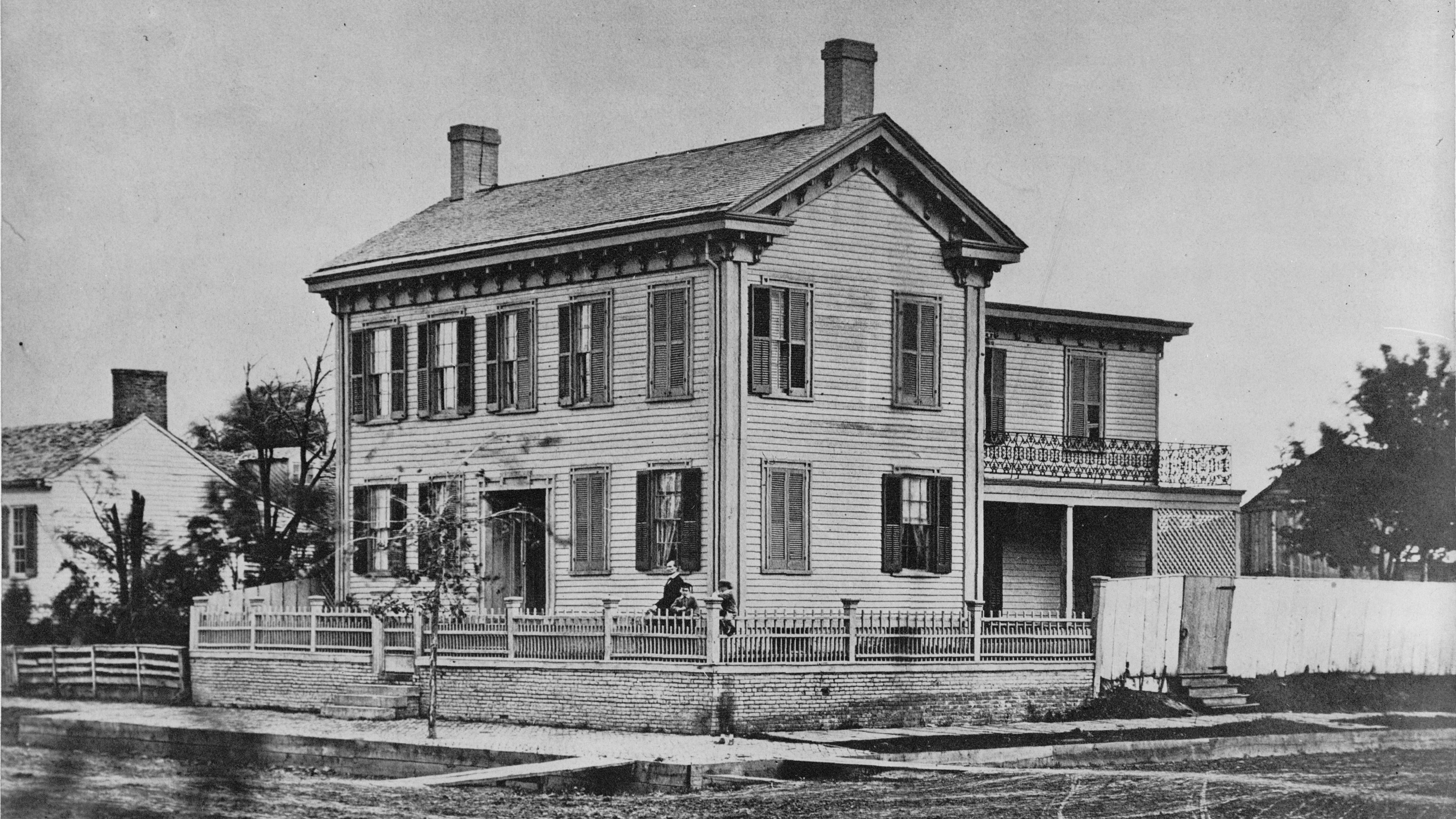 Black and white historic photo of the Lincoln Home with Abraham Lincoln and two of his boys behind t