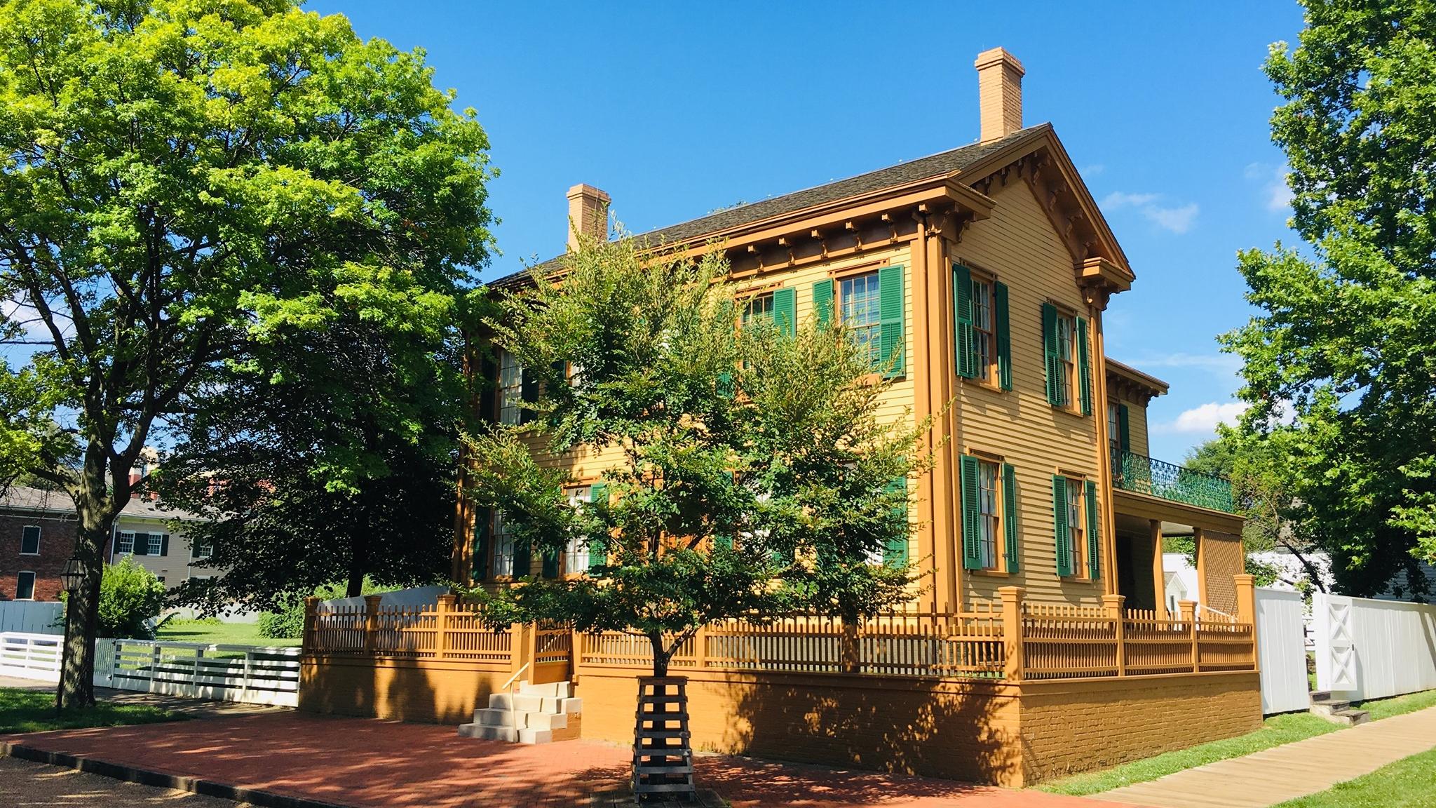 2 story wooden house with tan-yellow siding, coffee-colored trim, and dark green shutters
