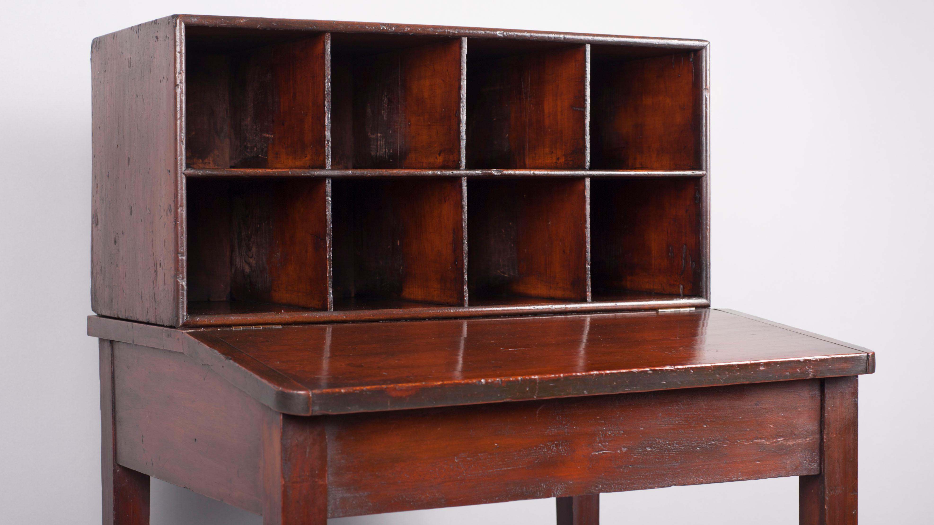 Photo of a small wooden desk with set of pigeonhole cubbies in two rows of 4 along back of desk