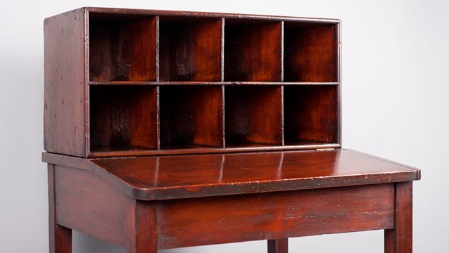 Photo of a small wooden desk with set of pigeonhole cubbies in two rows of 4 along back of desk