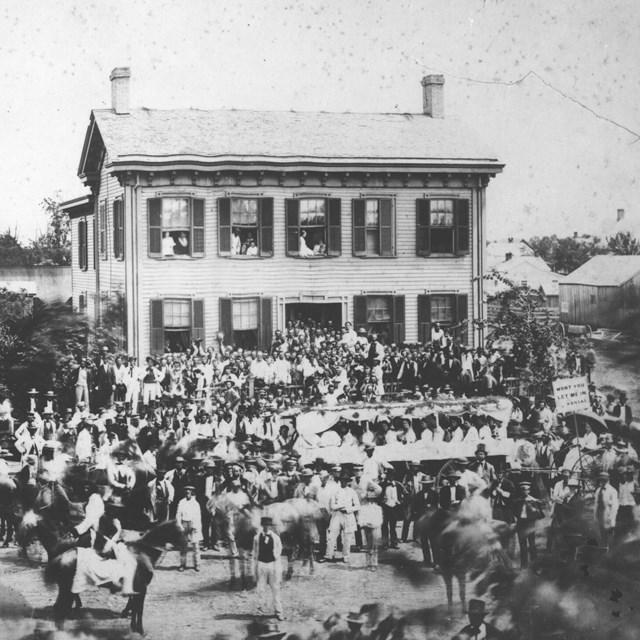 photo of Lincoln Home with large crowd of people standing on street and around house, parade