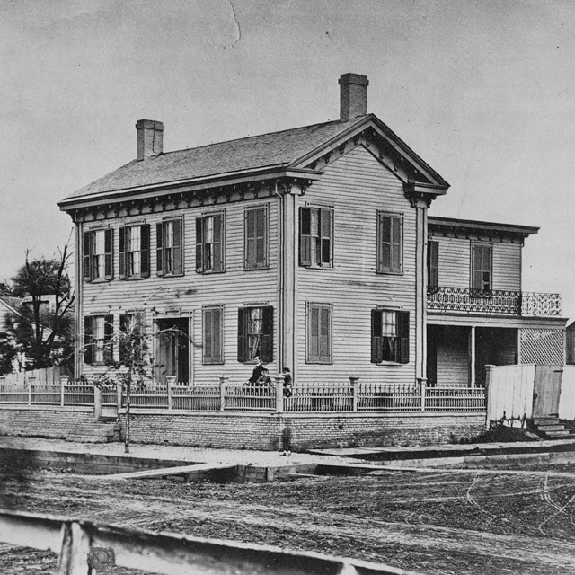 Black and white photo of the Lincoln Home, a 2-story wood house with dark shutters, 2 chimneys