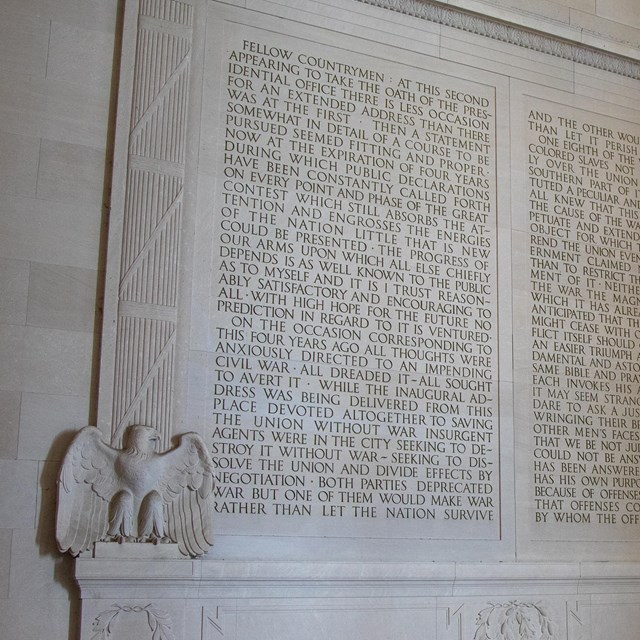 A wall of text carved into the stone, flanked by eagles.