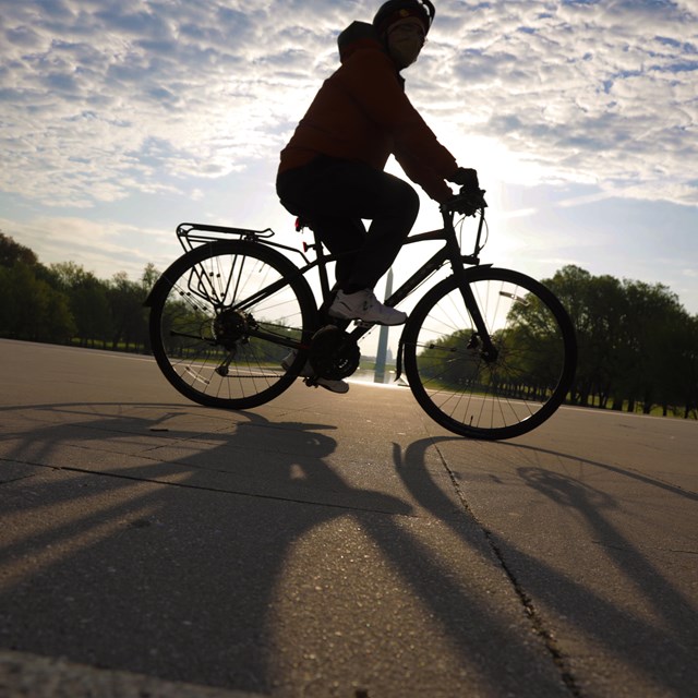 A person riding a bike on a paved sidewalk with the Washington Monument in the distance.