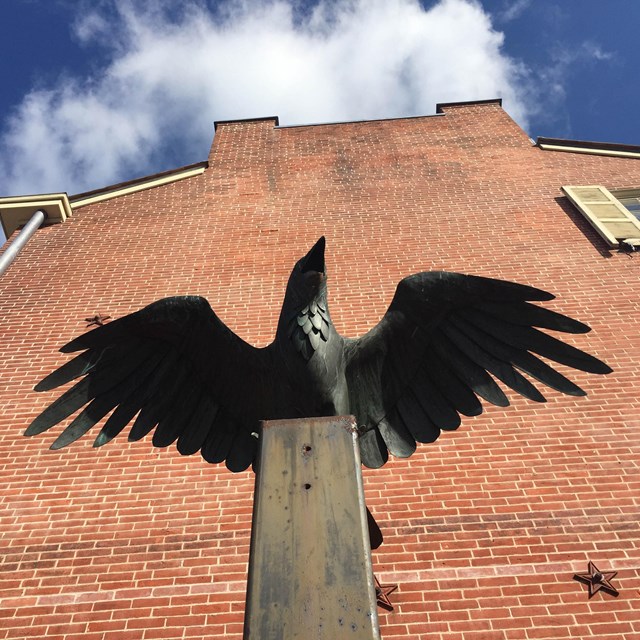 Statue of a raven next to a brick house