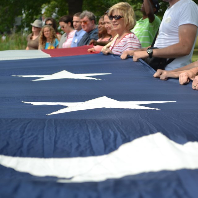 Line of hands holding a large US flag