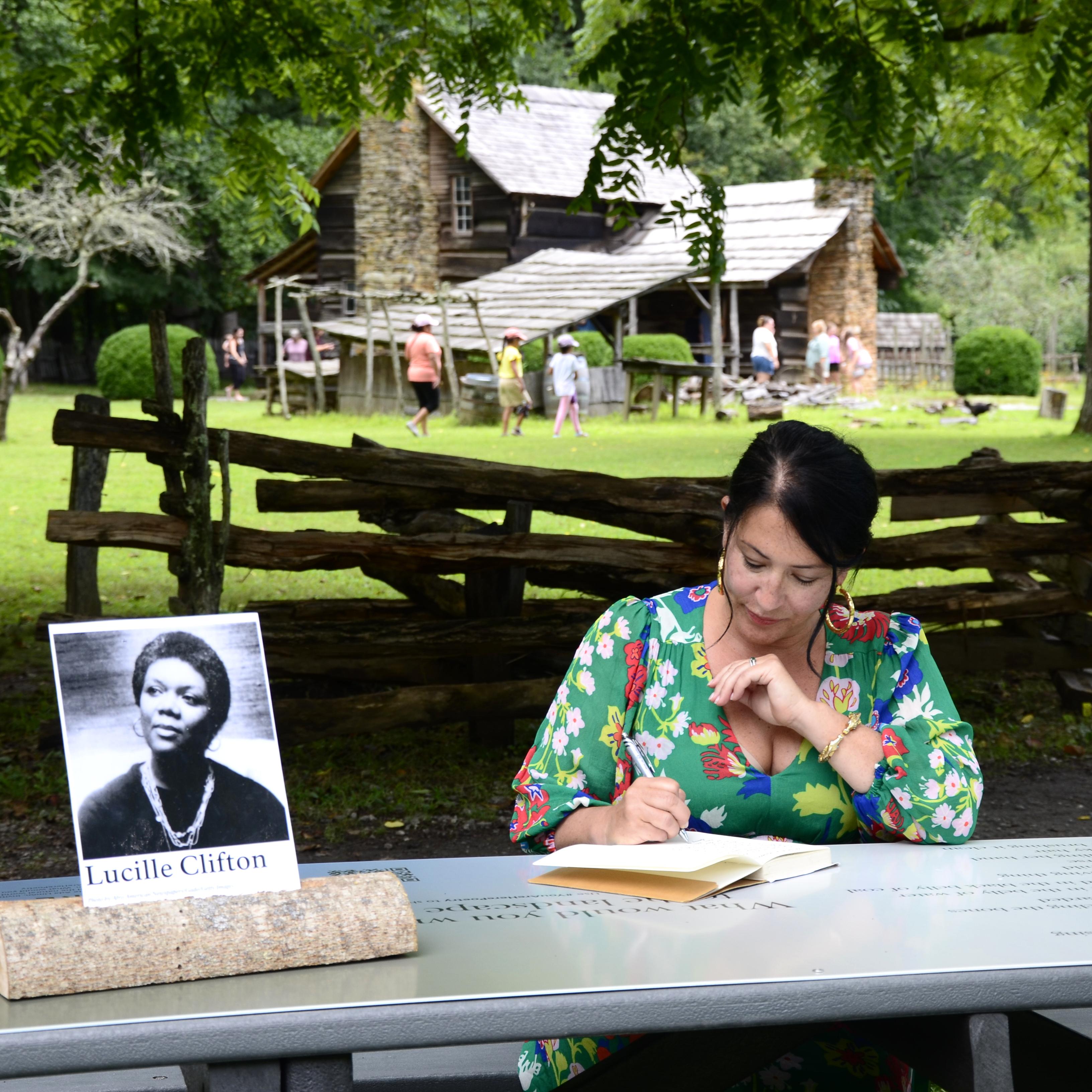 A person writing at a picnic table covered by a poem and an upright photo of the poet.