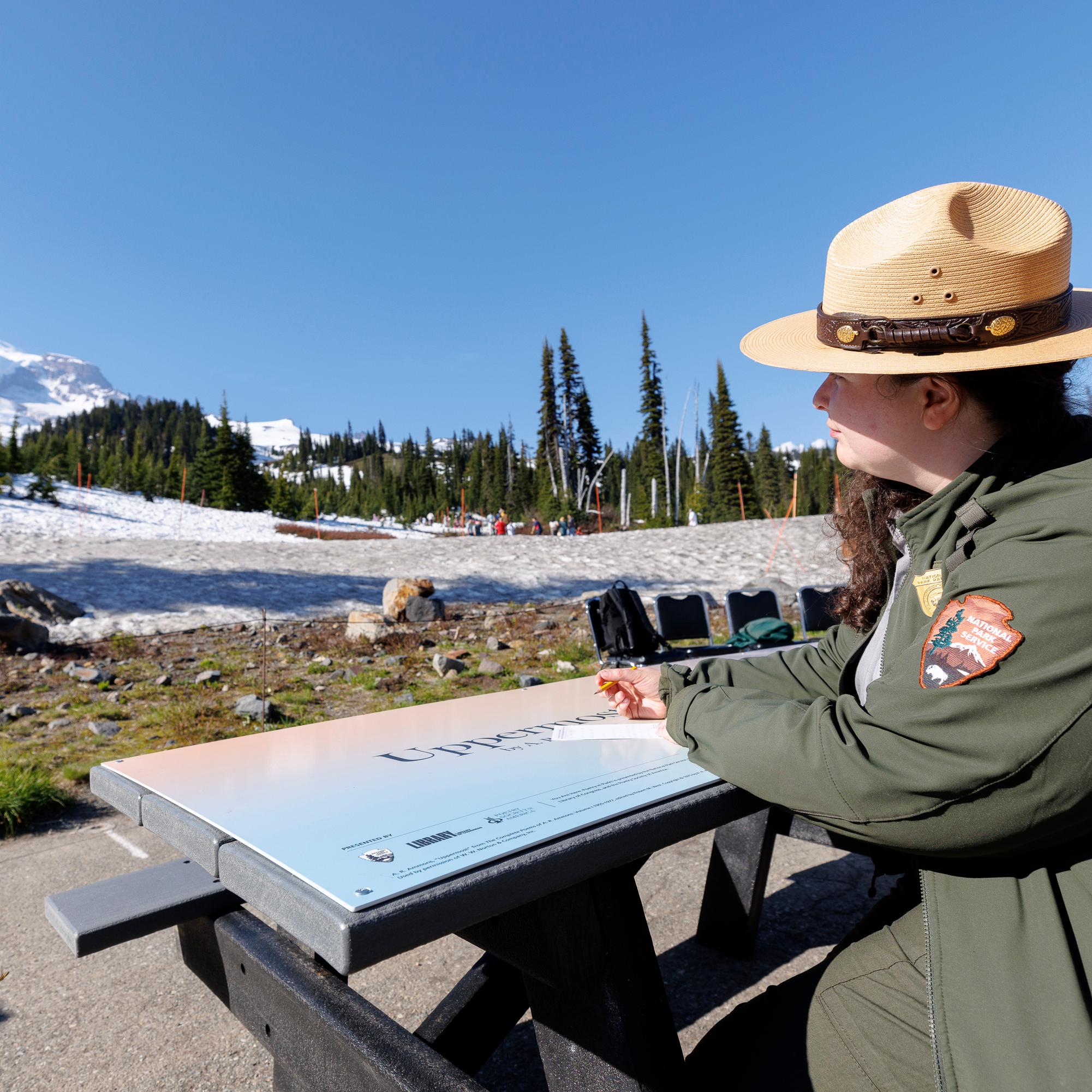 A park ranger writes at a picnic table covered with a poem outside.
