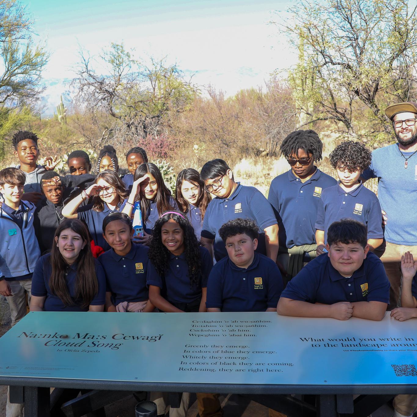 A group of students in front of a picnic table with a poem on it.