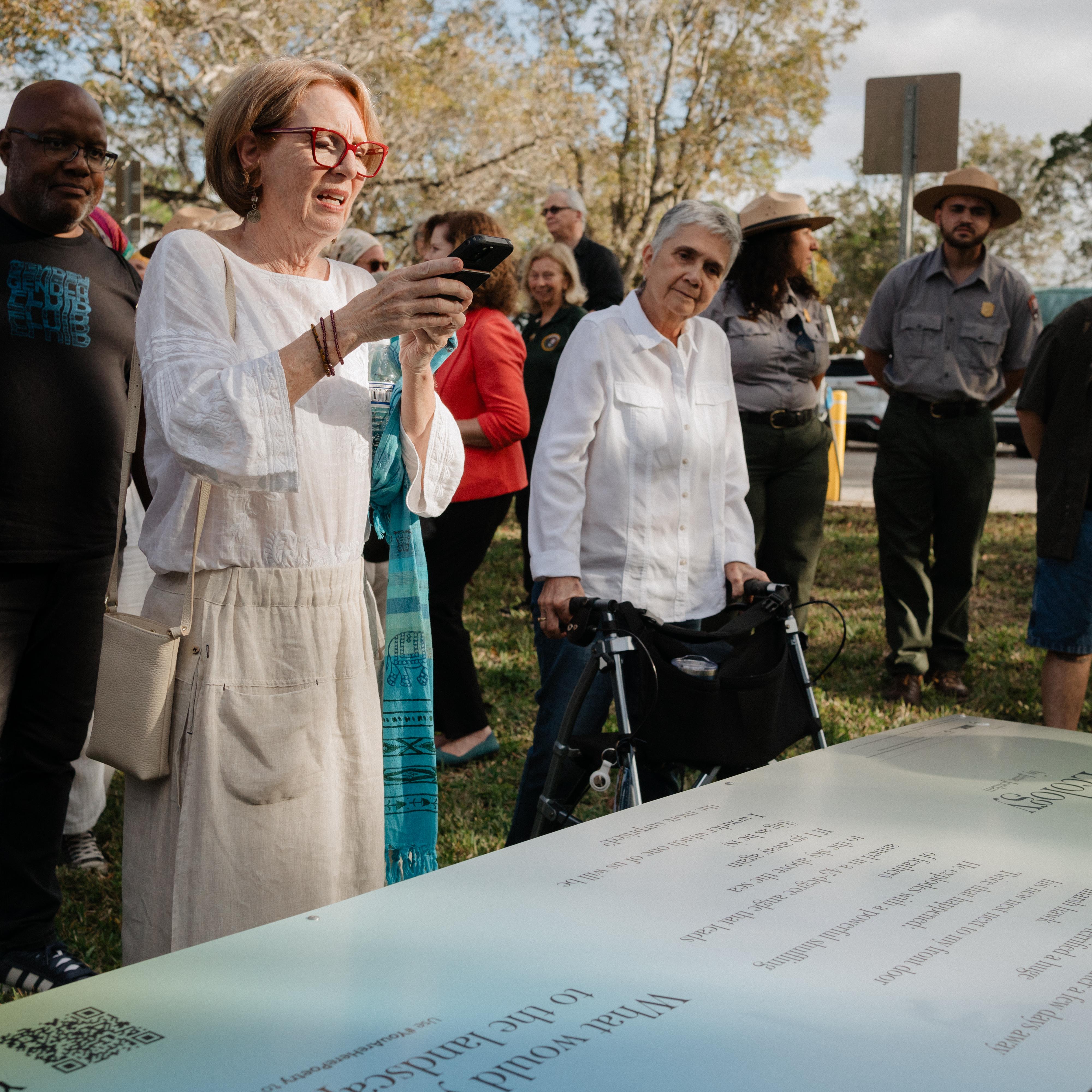 A group of people looking at a newly unveiled picnic table feature a poem on the top.