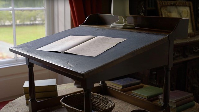 Historic elevated wooden writing desk by a window with two pieces of paper open on it