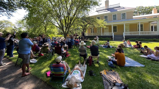 Crowd seated on chairs and blankets on lawn to watch concert