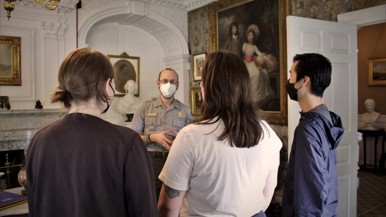 Visitors with backs to the camera, ranger facing camera in a Victorian parlor