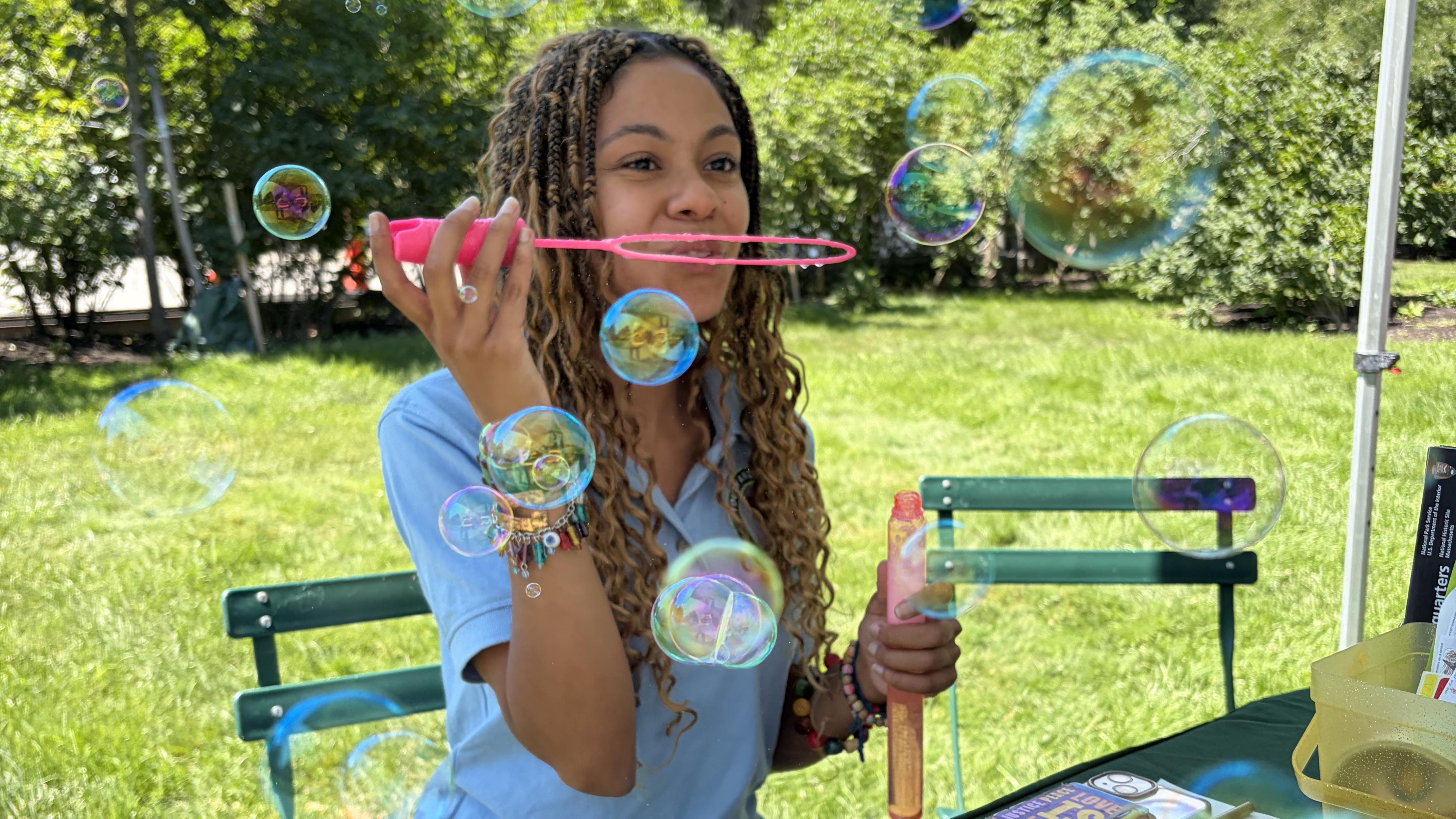 Young woman in a blue polo shirt blows bubbles outdoors.