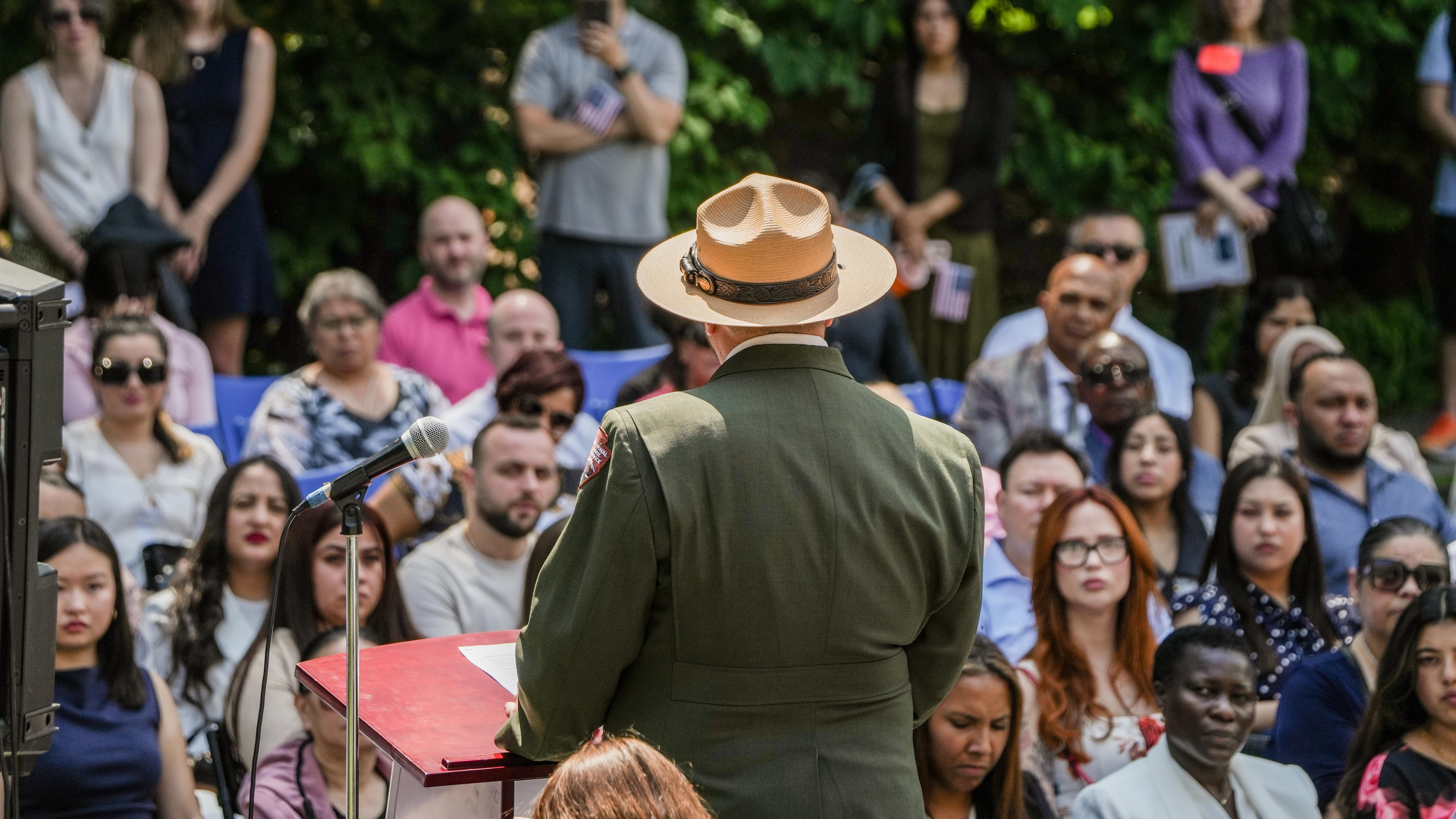 Park ranger, seen from behind, faces a seated outdoor crowd.