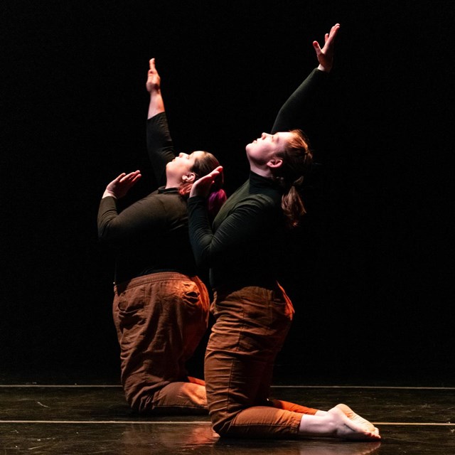 Two dancers kneeling with arms raised