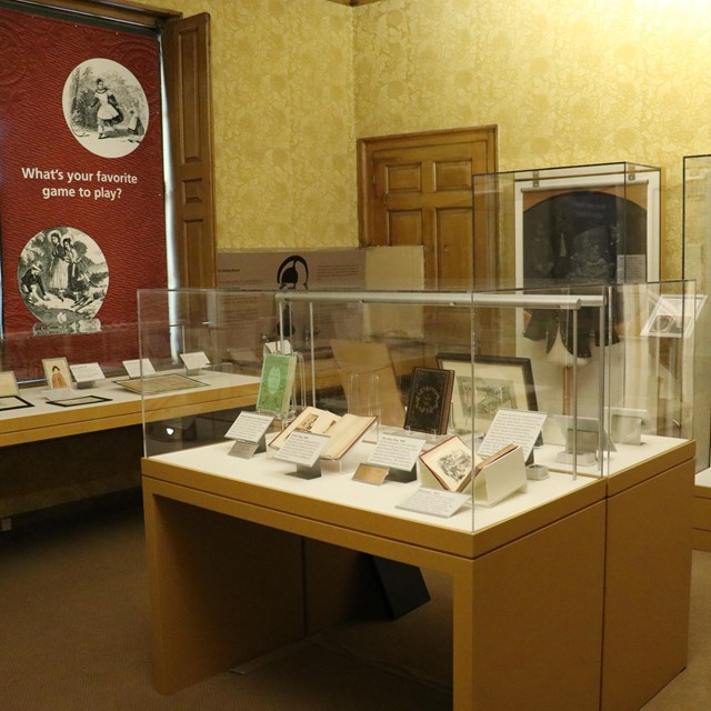 Room in historic house with exhibit cases of books and clothing