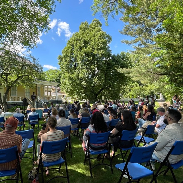 Crowd seated outdoors listening to a poetry reading