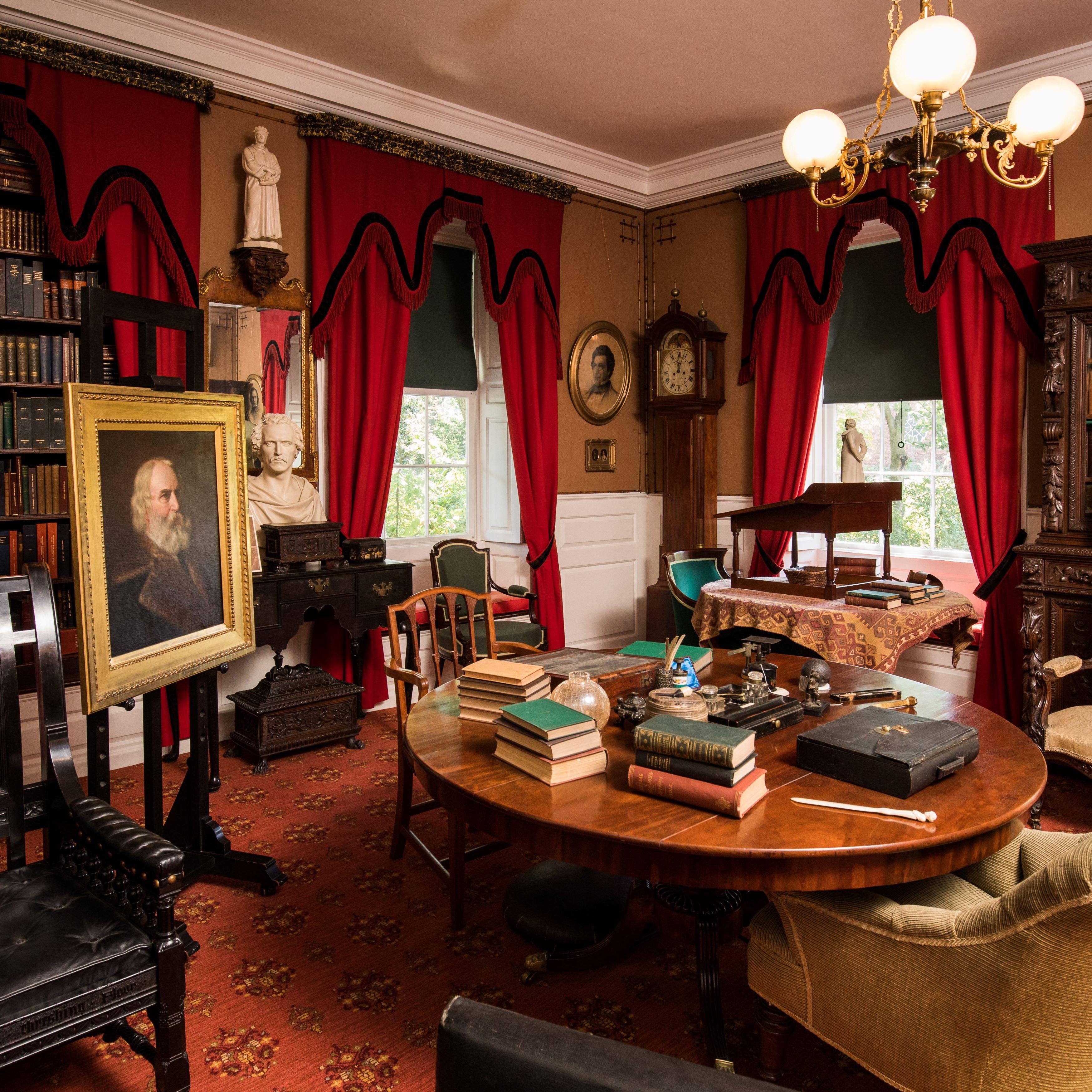 View of a study with a round center table cluttered with books and writing implements.
