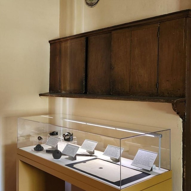 Room in historic house with exhibit cases of books and clothing