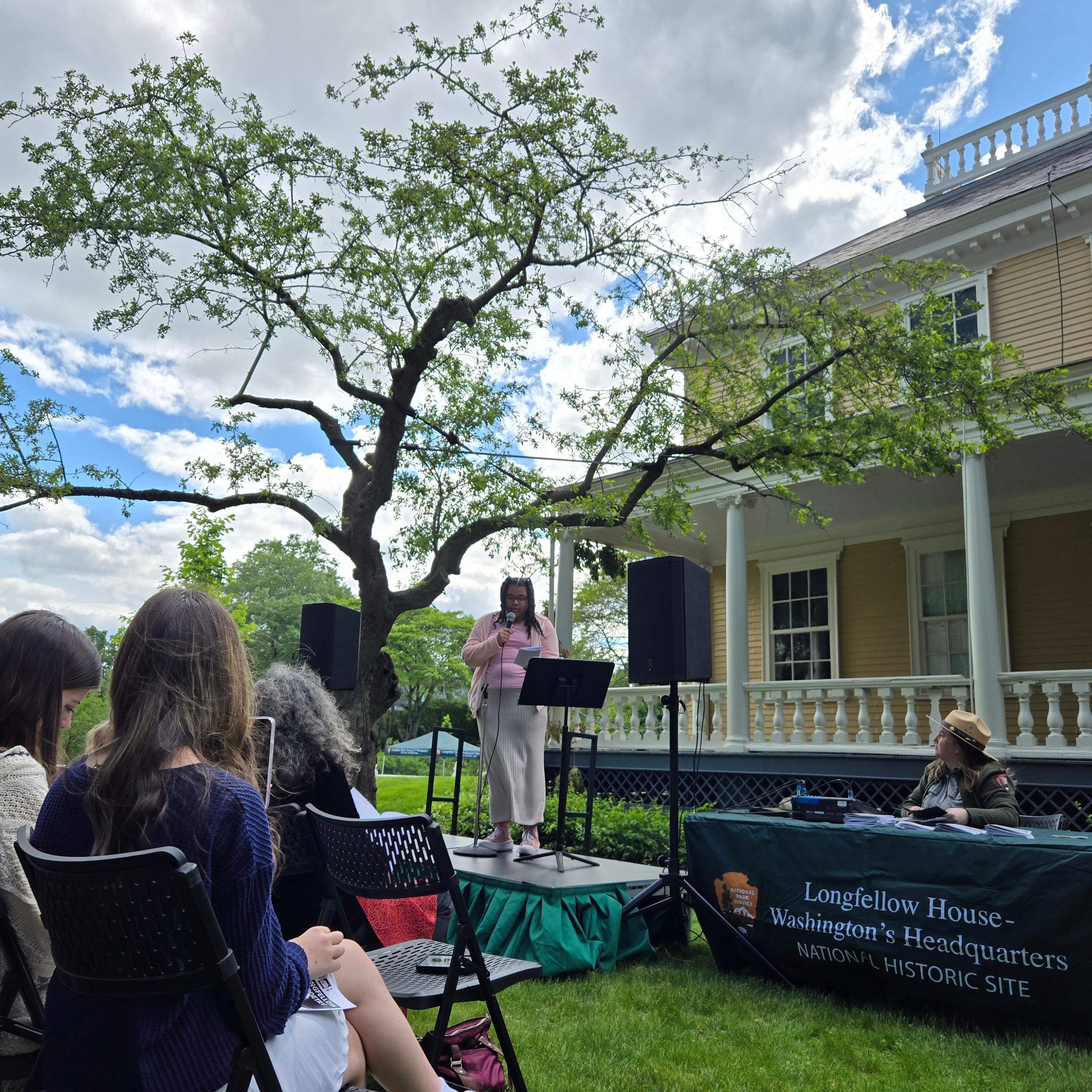 Young poet reads on an outdoor stage as audience looks on