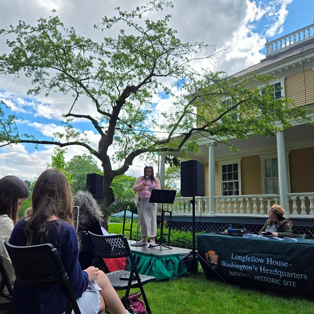 Young poet reads on an outdoor stage as audience looks on