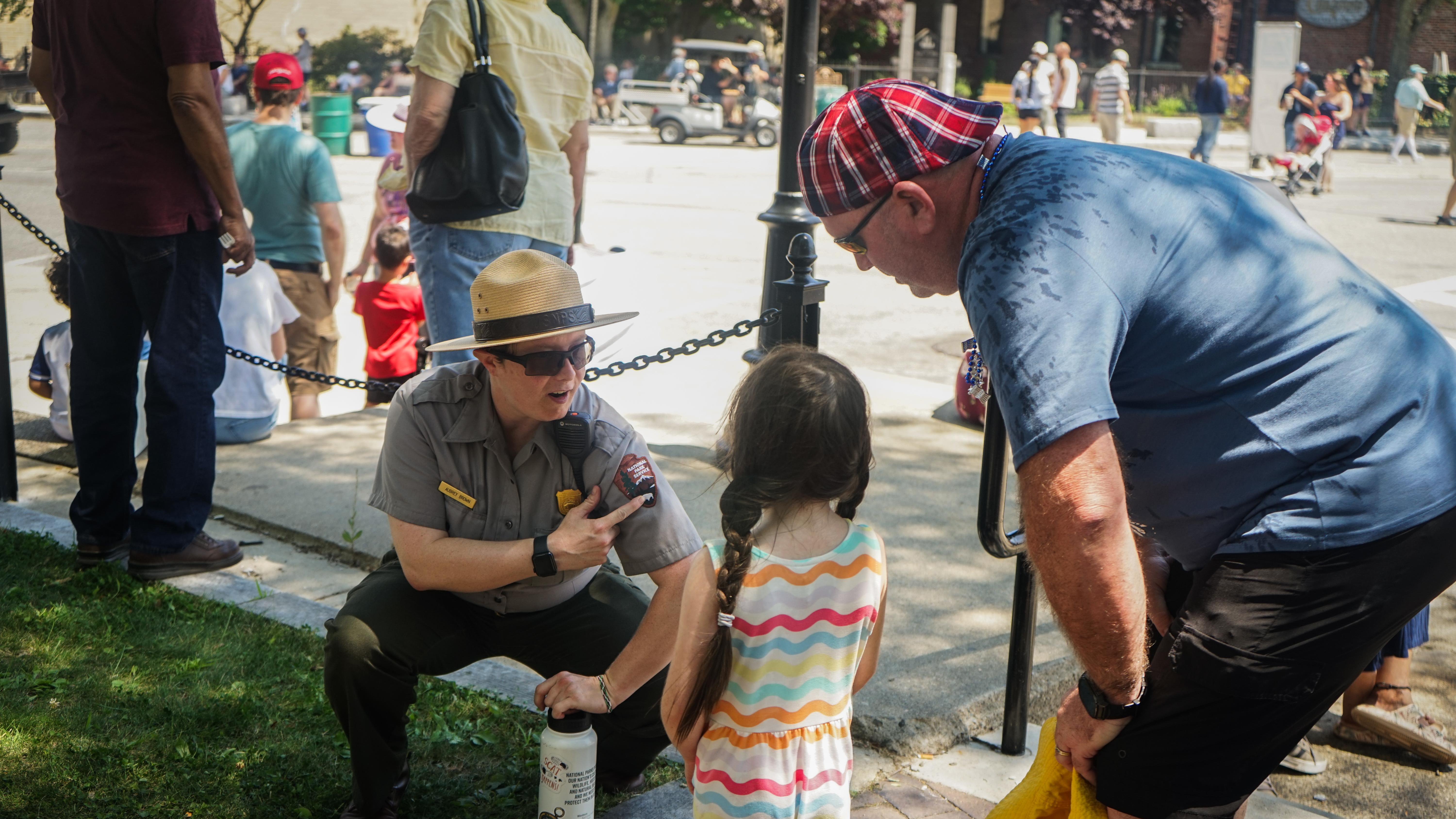 A ranger points out the arrowhead on their uniform to a child and watching adult