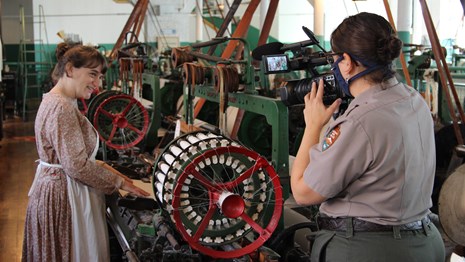A park ranger and a woman in costume film a video in a historic weave room.