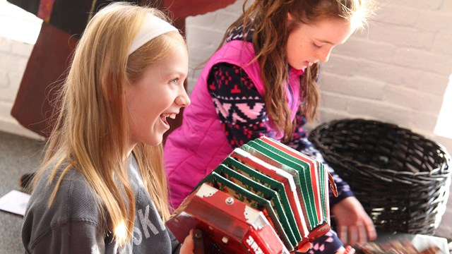 Two smiling girls sit on the floor playing with an accordion