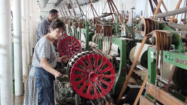 A weaver stands by a row of power looms