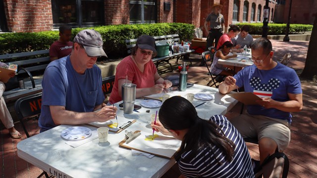 Participants sit around a table with painting supplies