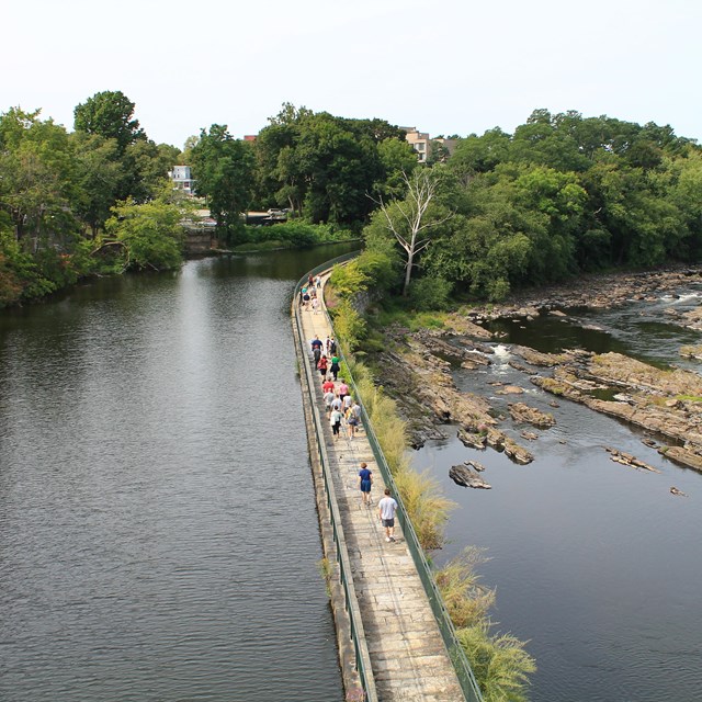 A group of people on a walkway between a canal and a river