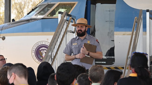 A ranger speaks to a group of children in front of a jet.