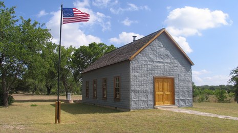 A flag flies outside a small, blue building.