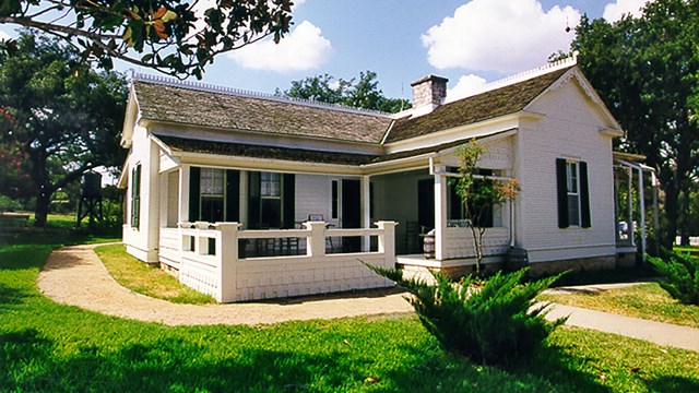 A small, one-story, white frame house shines in the bright summer sun.