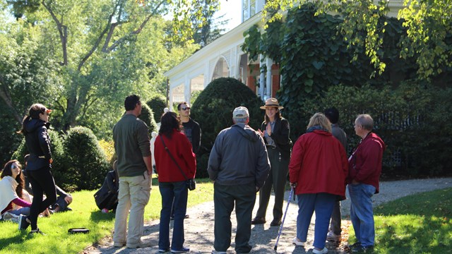 Ranger talks to a group of people in front of red brick mansion