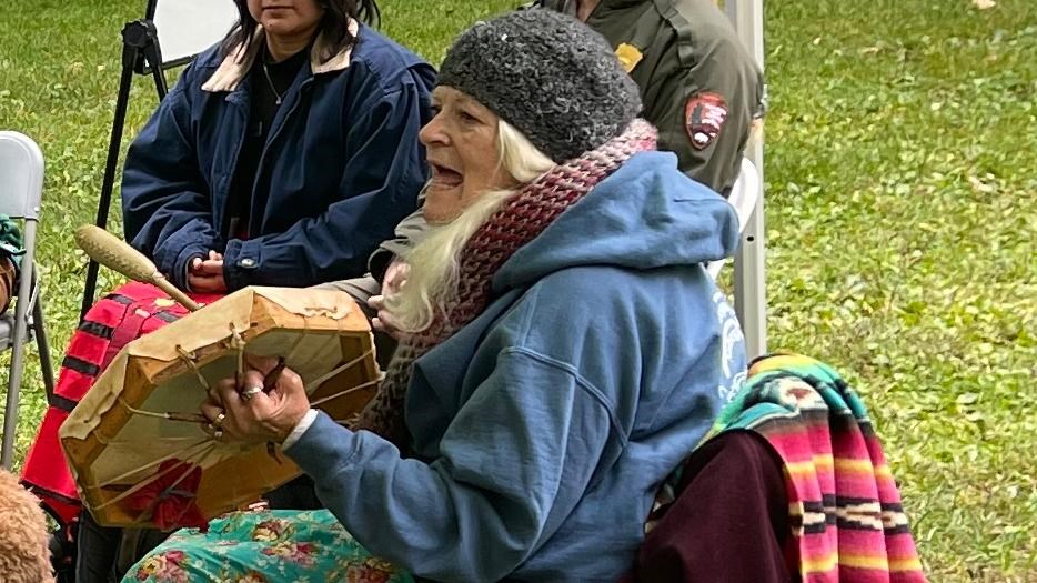 A group of people sit in a circle and listen to an Abenaki culture bearer