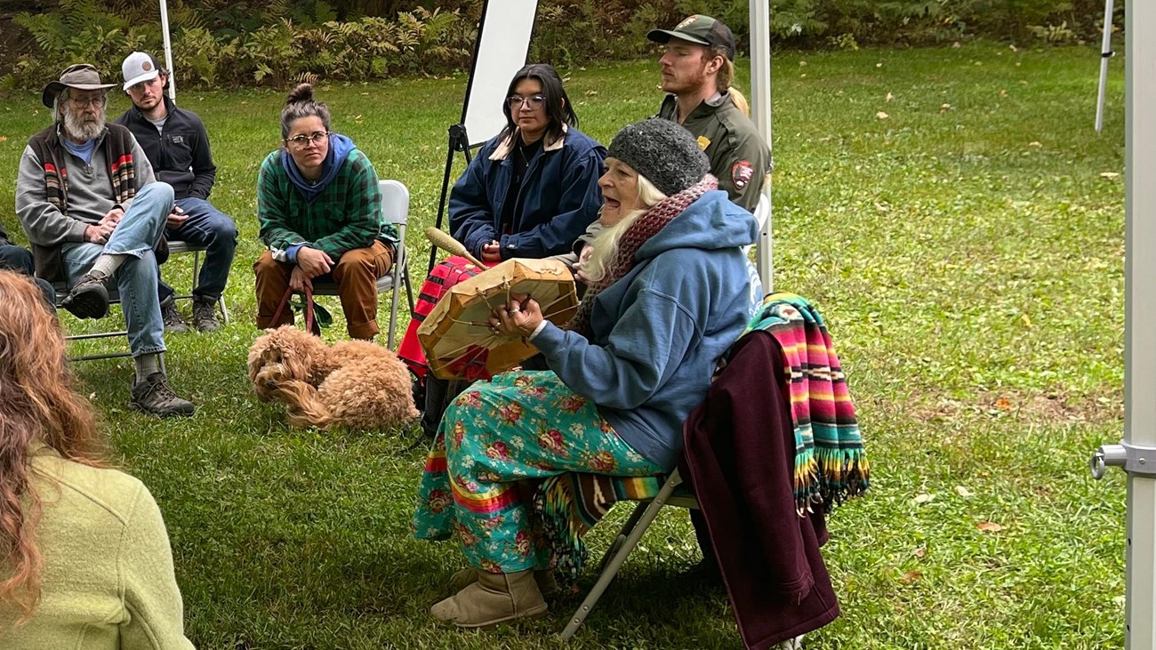 A group of people sit in a circle and listen to an Abenaki culture bearer